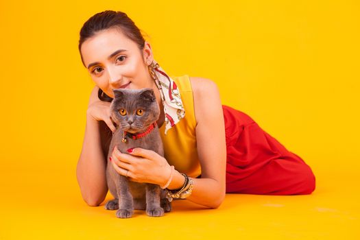 Beautiful young woman with his adorable cat in studio over yellow background.