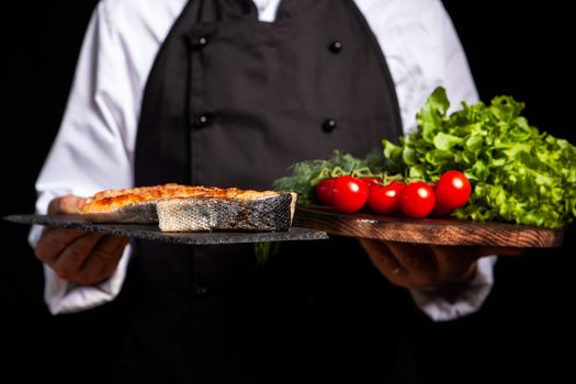 Chef holding two countertops one with fried salmon and the other with tomatoes and salad. Salmon rounds and close-up