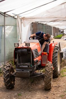 Young farmer sitting on a tractor in a greenhouse. Rural ocupation