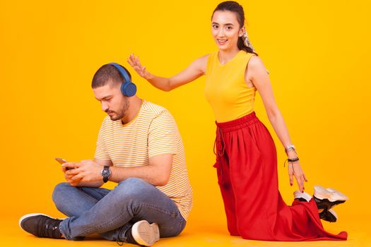 Boyfriend using his phone while girlfriend trying to get his attention. Couple sitting on studio floor.