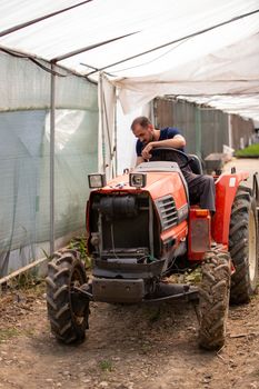 Young farmer trying to start a tractor in a greenhouse. Rural activity