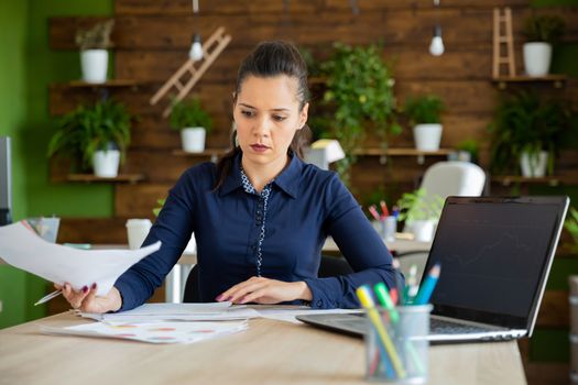 Beautiful caucasian businesswoman analyzes some business charts near a laptop
