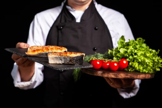 Plate with cooked salmon held in cook's hand. Plateau with greenery and tomatoes