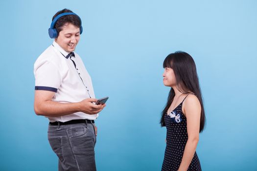 Smiling caucasian boyfriend with headphones ignoring his asian girlfriend. Interracial couple.