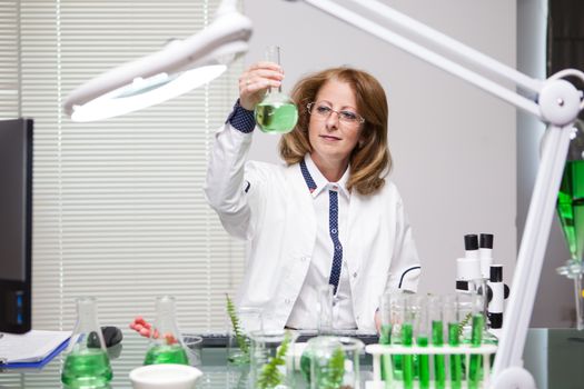 Portrait of middle age female scientist holding solutions for vegetables growth. Advanced technology in science laboratory.