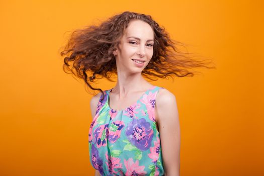 Cheerful young woman shaking her gorgeous hair in studio over orange background. Lovely summer dress.