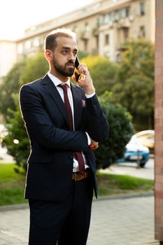 Caucasian businessman talking on the phone at sunset in the city. Business style and street view