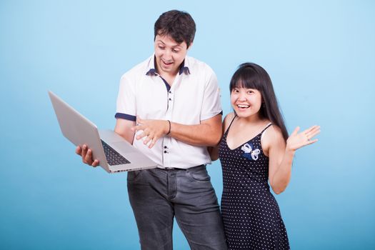 Caucasian husband showing his asian wife something exciting on laptop in studio. Interracial couple.