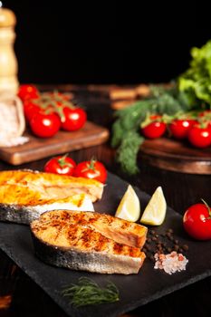 Grilled salmon served on a stone platter with slices of lime. Close-up