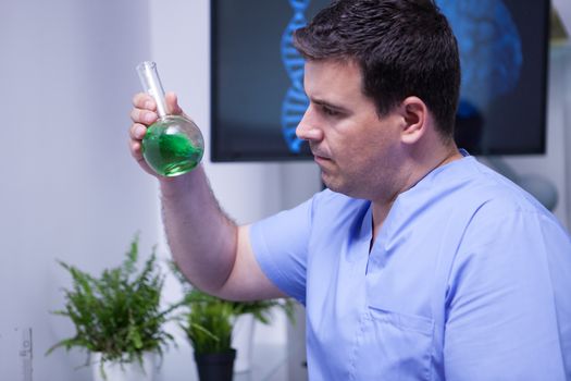Young male scientist in uniform looking at a green solution in a test tube. Science in human health.