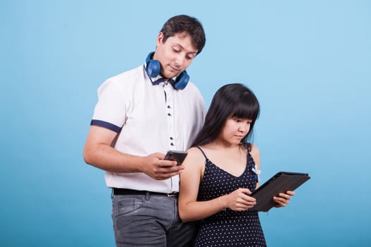 Caucasian boyfriend and asian girlfriend browsing on tablet and phone. Interracial couple.