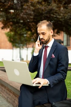 Business man talking on the phone and working on the laptop outside. Business style and professional attitude