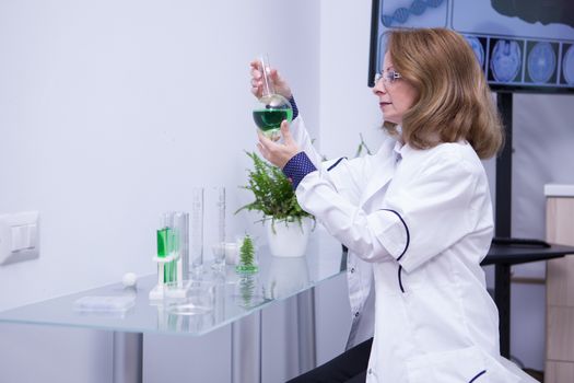 Mature female biologist looking at a green solution in her research lab. Adult scientist.