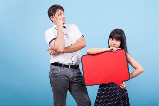 Thoughtful interracia couple looking at the camera in studio. Asian girl holding blank bubble thought.