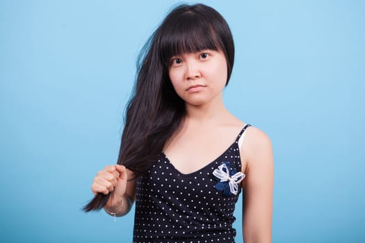 Portrait of asian girl with serious expression pulling her hair. Young asian female.
