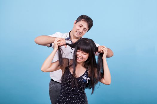 Caucasian young man teasing his asian girlfriend pulling her hair. Interracial couple.