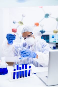 Young researcher holding a pipette and a glass container in his hand. Blue liquid and tube laboratory