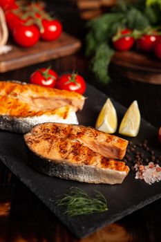 Cooked salmon rounds placed on a platter with a few slices of lime beside it. Tomatoes and salad on the background