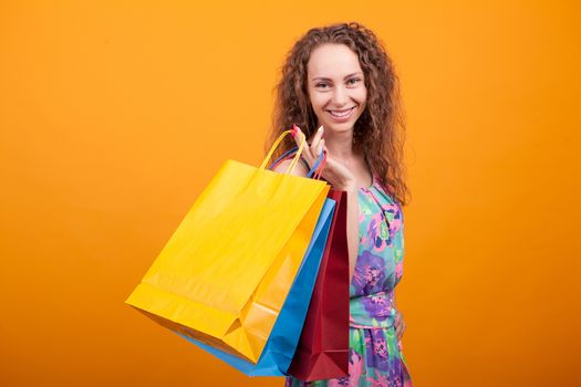 Stylish caucasian woman smiling and holding shopping bags over orange background.
