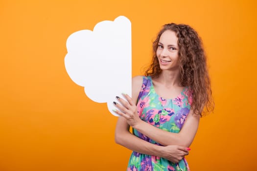 Gorgeous young woman holding an empty placard in studio over orange background. Empty bubble thoughts.