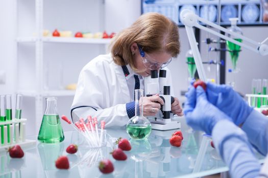 Mdiddle age female scientist with protection glasses looking into her microscope. Research lab.