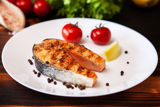 Cooked salmon ring served on white lemon and pepper plate. Tomatoes and salad