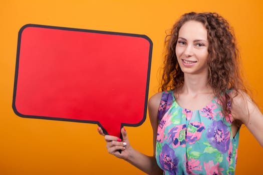 Smiling woman holding an empty banner in studio over orange background. Copy space available.