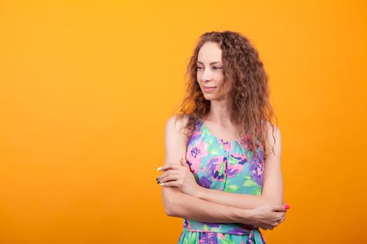 Young woman posing in studio keeping her arms corssed over orange background.