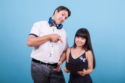 Asian girlfriend holding tablet and caucasian boyfriend pointing at it in studio. Interracial couple.
