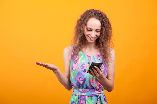 Young girl looking confused at her phone over orange background. Girl with curly hair.