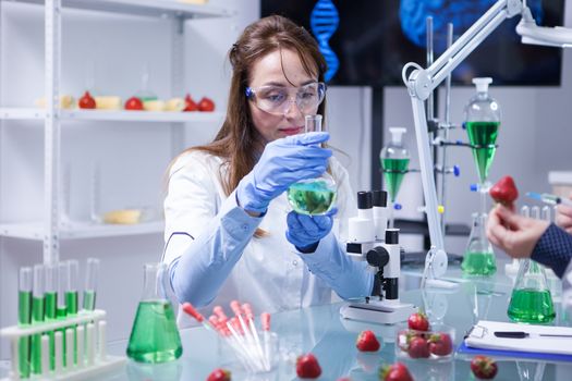 Middle age scientist woman wearing protection glasses in a research laboratory. Test tubes. Strawberries.