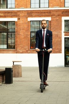 Young businessman in a suit riding an electric scooter in a business district. Street and office building