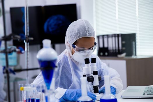 Female scientist analysing blue substance in a research laboratory on microscope.