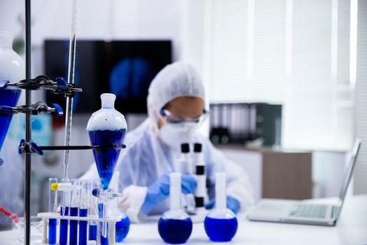 Close up of smoking blue solution in test tubes and scientist in the background working.