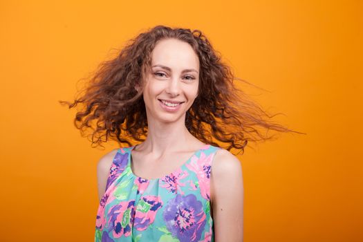 Beautiful woman portrait smiling and shaking her curly hair in studio over orange background.