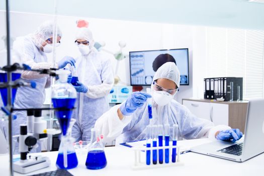 Young team of chemists examines a blue substance that is in the tube. Surrounded by scientific equipment
