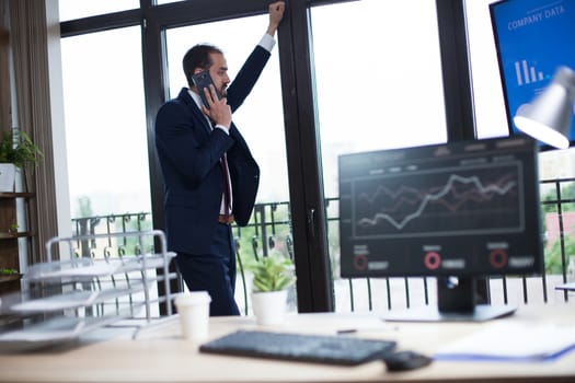 Handsome bearded businessman looking on the window and having a business conversation the phone. Young entrepreneur.