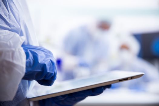 The chemist in blue gloves uses a tablet that holds it in his hand. Close up