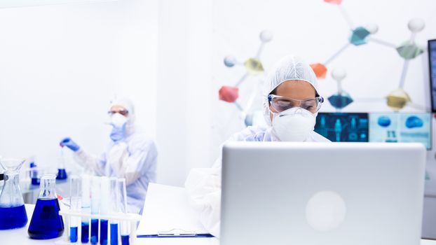 Scientist woman working on laptop in the laboratory. Surrounded by tubes and beakers