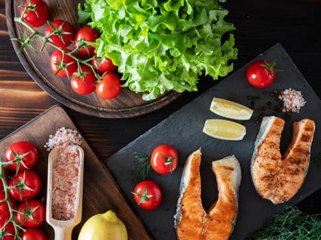 Top view of salmon arrangement with salad and tomatoes on wooden and stone trays