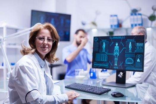 Portrait of middle age female engineer looking at the camera in a science laboratory. Technician working with test tubes in the background.