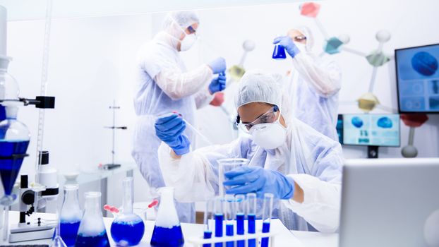 Three scientists analyzing several containers with blue liquid. High-end laboratory
