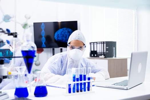 The female chemist looks at a tube holder with a blue liquid. Chemistry and science