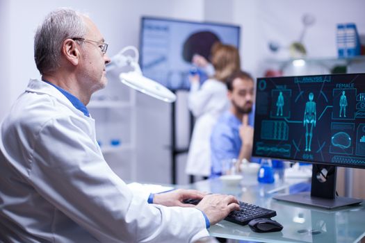 Experienced senior scientist typing the data in computer from last experiment on human body. Inovation center.