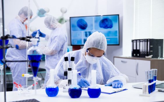 Female scientist with microscope near and smoking blue solution in test tubes working in a research laboratory.