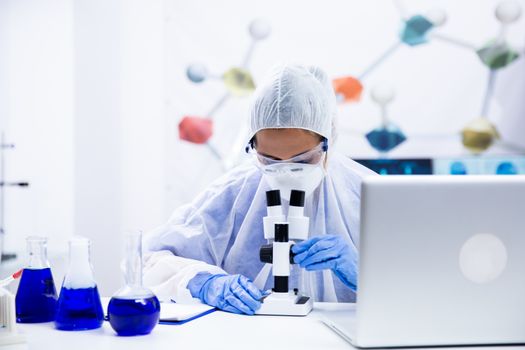 Scientists women in blue glove adjusting their microscope. Test tubes with smoking blue solution.