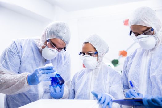 Team of scientist analysing a smoking blue solution from a test tube in a modern laboratory.