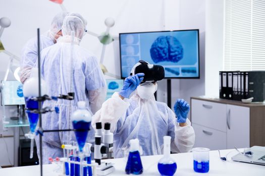 Female scientist using virtual reality simulation for scientific research in a moder laboratory and reactive blue liquid in test tubes.