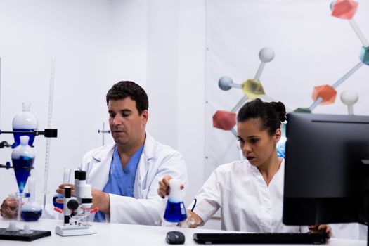 Team of researchers wearing their coat in research laboratory. Female researcher looking at test tube with blue liquid.
