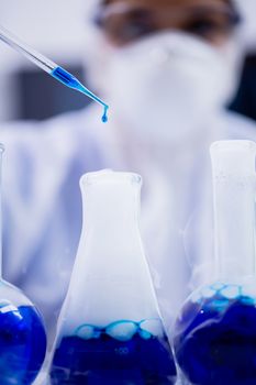 Close up of female scientist with blue solution dropping from pipette in a modern laboratory.